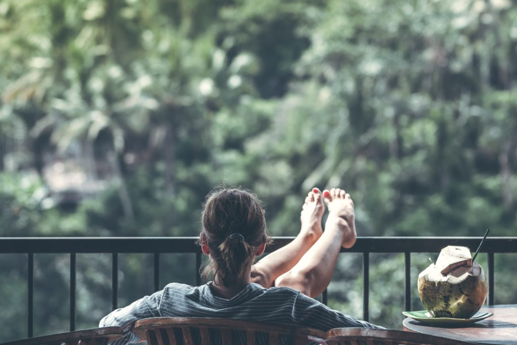 A person sits with an open green coconut next to her on a balcony overlooking a rainforest. Photo by Artem Beliaikin from Pexels.