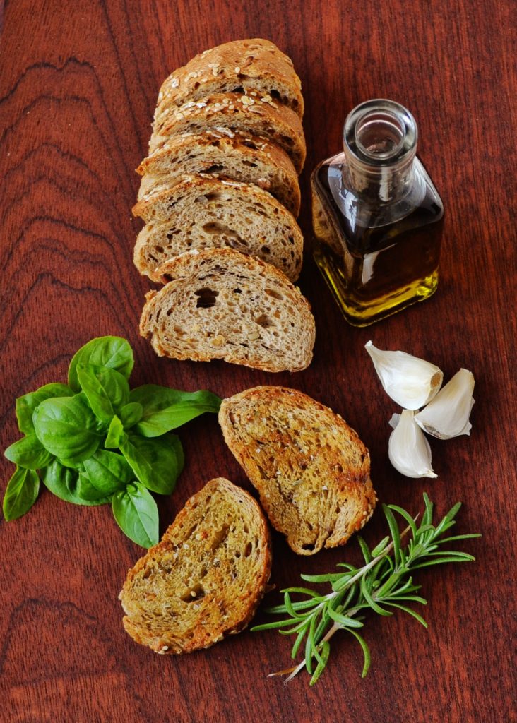 Organic olive oil and fresh baked bread presented with basil, rosemary, and garlic. Photo by Dana Tentis from Pexels.